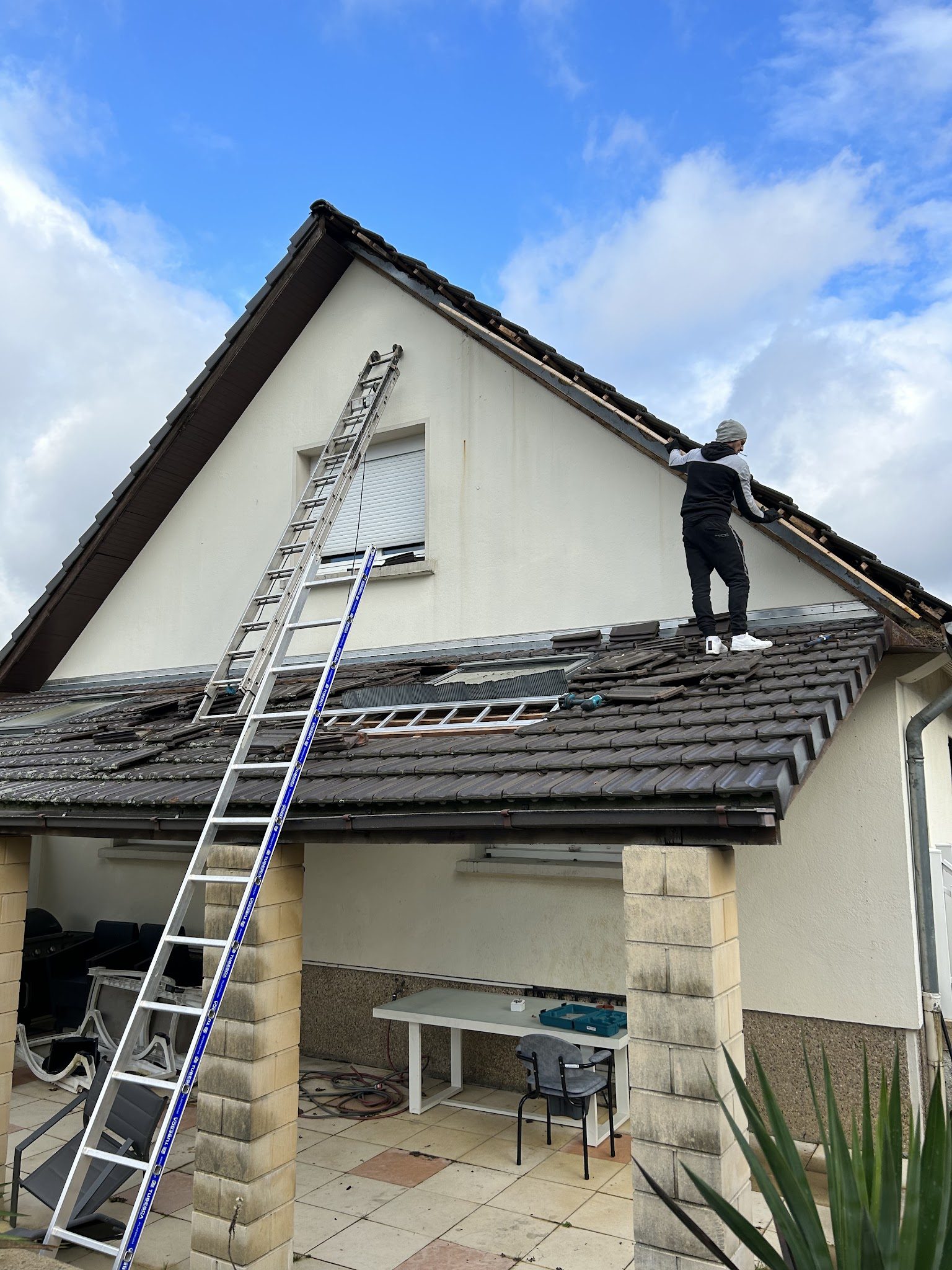 Un couvreur KD Toiture retire les tuiles d'un pignon, l'échelle posée contre la maison